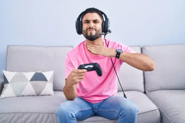 西班牙裔年轻人手握电视游戏控制器 坐在沙发上 手拿刀割喉 用愤怒的暴力威胁挑衅 — 图库照片