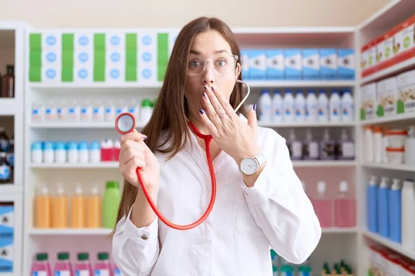 Beautiful Brunette Woman Working Pharmacy Drugstore Holding Stethoscope Covering Mouth — Stock Photo, Image