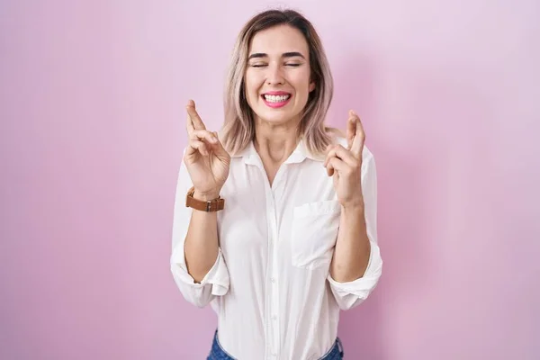 Young Beautiful Woman Standing Pink Background Gesturing Finger Crossed Smiling — Foto de Stock