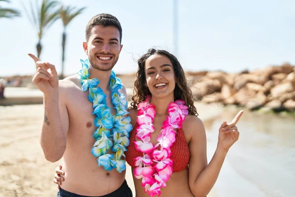 若いですヒスパニック系のカップル身に着けていますHawaiianネックレスでビーチ笑顔幸せなポインティングで手と指で側面 — ストック写真