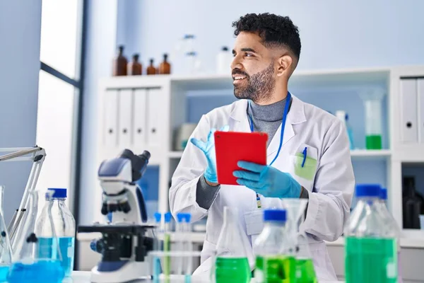 Laboratuvarda dokunmatik ped kullanan genç bir İspanyol bilim adamı üniforması giyiyor.