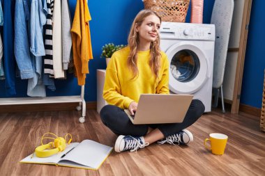 Young blonde woman waiting for washing machine studying at laundry room