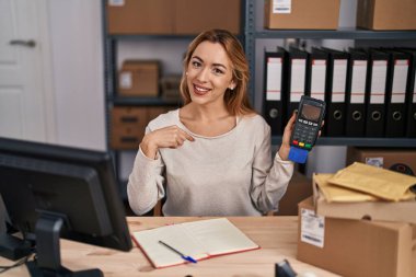 Hispanic woman working at small business ecommerce holding credit card and dataphone pointing finger to one self smiling happy and proud 