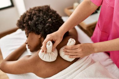 Genç Afrikalı Amerikalı kadın güzellik merkezinde Tayland çantalarıyla sırt masajı yaptırıyor.