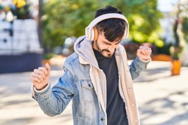 Young hispanic man smiling confident listening to music and dancing at park