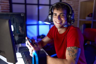 Young hispanic man streamer playing video game using joystick at gaming room