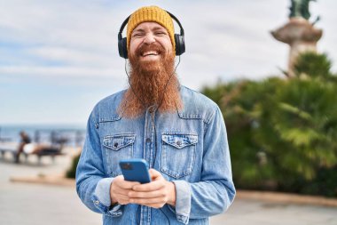 Young redhead man smiling confident listening to music at street