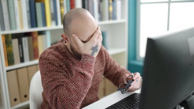 Üniversite sınıfında bilgisayar kullanan kel bir genç.