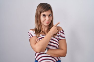 İzole edilmiş arka planda dikilen genç İspanyol kadın el ile işaret ederek reklamını yapıyor, ciddi ve sakin bir yüz ifadesi. 