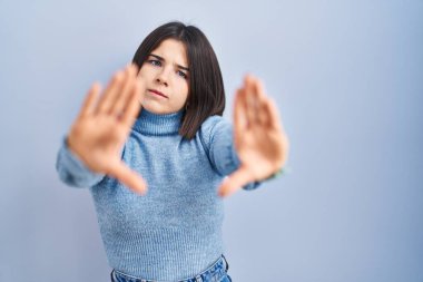 Mavi arka plan üzerinde duran genç İspanyol kadın el ve parmakları kullanarak çerçeve yapıyor, kamera bakış açısı. 