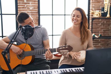 Erkek ve kadın müzisyenler müzik stüdyosunda klasik gitar ve tef çalıyor.