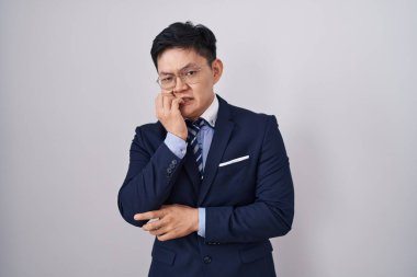 Genç Asyalı takım elbiseli ve kravatlı adam gergin ve gergin görünüyor. Ağzı tırnak yiyen eller. anksiyete. 