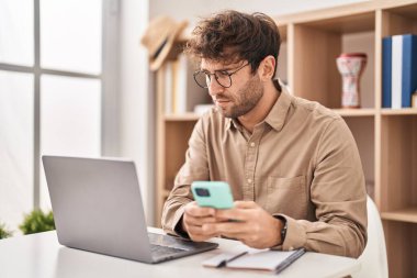 Ofiste çalışan akıllı telefon ve dizüstü bilgisayar kullanan genç bir iş adamı.