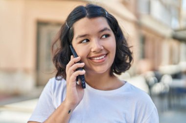 Gülümseyen genç bir kadın caddedeki akıllı telefondan konuşuyor.