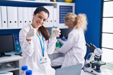 Laboratuvarda gülümseyen mutlu ve pozitif gülümseyen genç İspanyol kadın mükemmel ve onay işareti yapıyor. 
