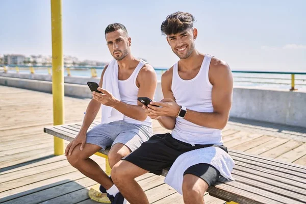 两只惊慌失措的男人用智能手机坐在海滨的长椅上 — 图库照片