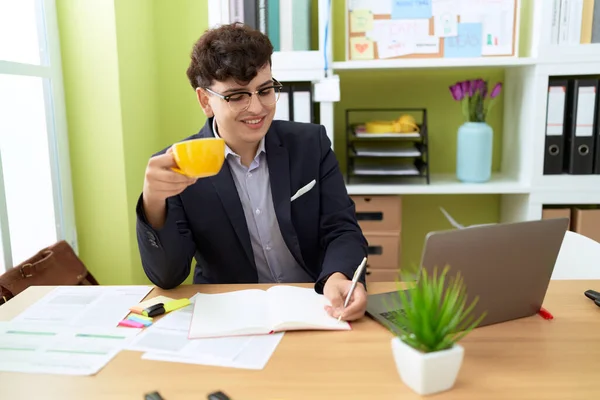 Non binary man business worker writing on document drinking coffee at office
