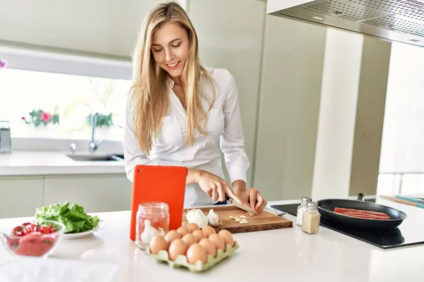年轻的金发女人在厨房用触摸板做饭 — 图库照片