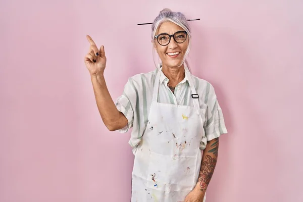 Middle age woman with grey hair wearing artist look smiling happy pointing with hand and finger to the side