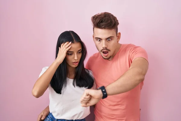 Young Hispanic Couple Standing Pink Background Looking Watch Time Worried — Stockfoto