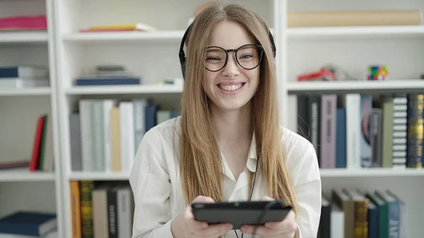 大学の教室で勉強するタッチパッドとヘッドフォンを使用して若いブロンドの女性学生 — ストック写真