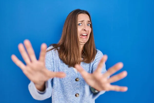 年轻的女人站在蓝色的背景上 害怕而害怕 用恐惧的表情 用手停止手势 震惊地大叫 恐慌概念 — 图库照片