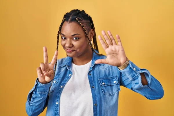 Африканская Американка Косичками Стоящая Желтом Фоне Показывающая Пальцами Номер Семь — стоковое фото