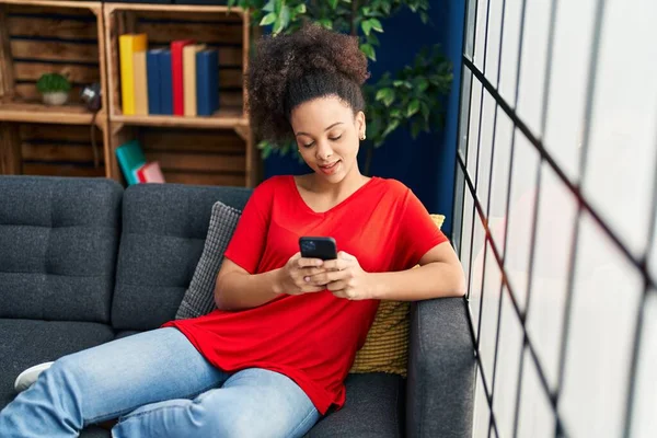 年轻的非洲裔美国女人坐在家里的沙发上用智能手机 — 图库照片