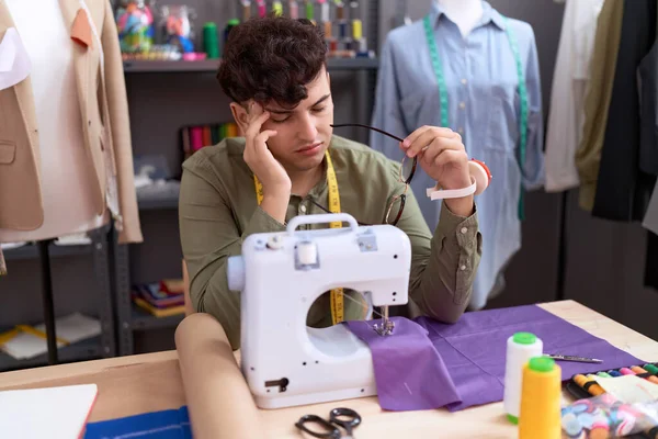 Non binary man tailor stressed using sewing machine suffering for headache at atelier