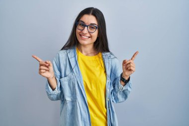 Mavi arka planda duran genç İspanyol kadın parmaklarıyla farklı yönleri gösteren kendine güvenle gülümsüyor. reklam için kopyalama alanı 