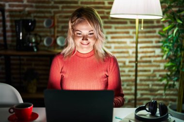 Sarışın kadın evde dizüstü bilgisayar kullanıyor. Yüzünde mutlu ve havalı bir gülümseme var. şanslı kişi. 