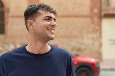 Young hispanic man smiling confident looking to the side at street