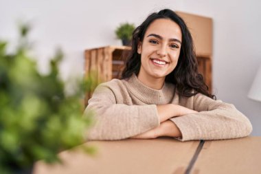 Genç İspanyol kadın gülümsüyor. Yeni evinde pakete yaslanıyor.