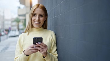Sokakta akıllı telefon kullanan, kendine güvenen genç sarışın kadın.