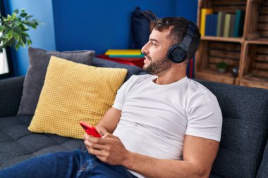 Genç İspanyol adam evdeki kanepede oturmuş müzik dinliyor.