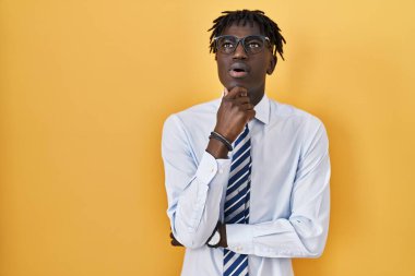 Sarı arka planda duran Afrikalı adam kameraya kendinden emin bir şekilde bakıyor kollarını kavuşturmuş ve çenesini kaldırmış gülümsüyor. Olumlu düşünmek. 