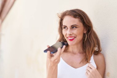 Genç, güzel, İspanyol bir kadın gülümsüyor ve caddede akıllı telefondan konuşuyor.