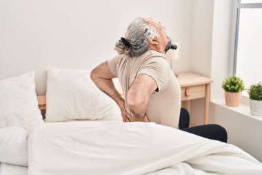 Middle age grey-haired man suffering for back injury sitting on bed at bedroom