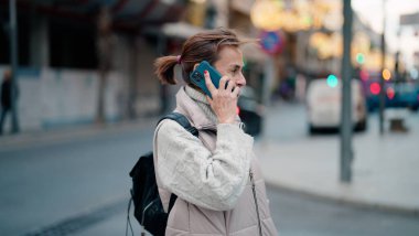 Orta yaşlı İspanyol kadın gülümsüyor. Akıllı telefondan konuşuyor.