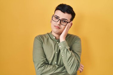 Non binary person standing over yellow background thinking looking tired and bored with depression problems with crossed arms. 