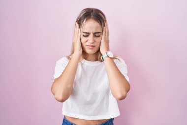 Young blonde woman standing over pink background with hand on head, headache because stress. suffering migraine. 