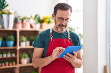Middle age man florist using touchpad with serious expression at florist