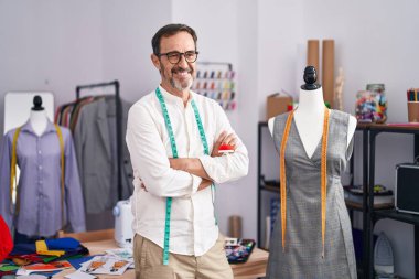 Middle age man tailor smiling confident standing with arms crossed gesture at tailor shop