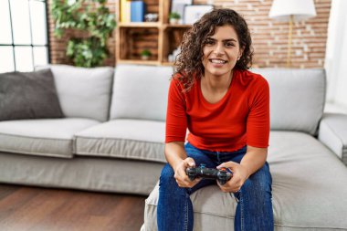Evde video oyunu oynarken kendinden emin gülümseyen genç Latin kadın.