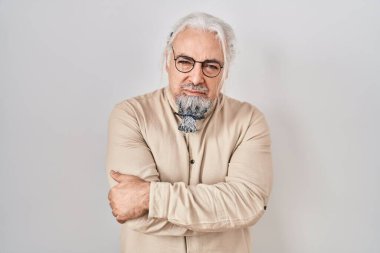 İzole edilmiş arka planda duran gri saçlı, kuşkucu ve gergin orta yaşlı bir adam. Yüzünde çapraz kollarla onaylamayan bir ifade var. negatif kişi. 