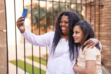 Mother and daughter hugging each other make selfie by smartphone at street