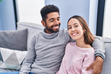 Erkek ve kadın çift evdeki kanepede oturup birbirlerine sarılıyorlar.