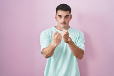 Yakışıklı İspanyol bir adam pembe arka planda duruyor. Yumruk savunma hareketleriyle dövüşmeye hazır. Kızgın ve üzgün bir yüz, sorundan korkuyor. 