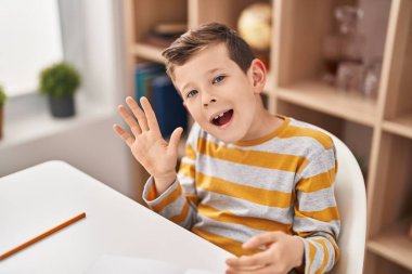 Blond child saying hello sitting on table at home