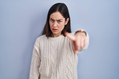 Genç esmer kadın mavi arka planda dikiliyor. Kameraya kızgın ve sinirli olduğunu gösteriyor. 